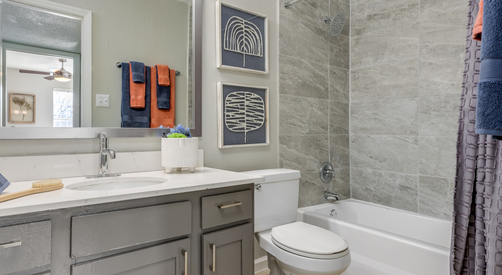 a bathroom with gray cabinets, white countertops and a shower at The Winslow